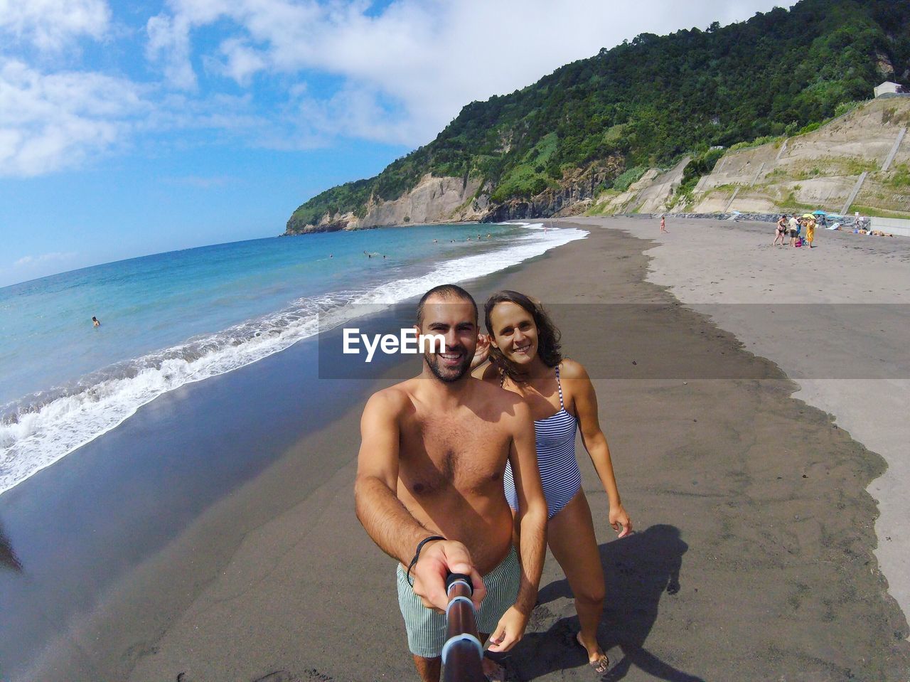 Portrait of happy couple taking selfie at beach on sunny day