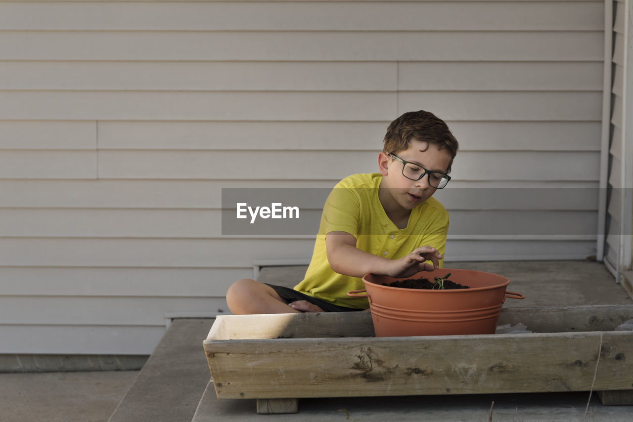 Boy planting sapling in flower pot at backyard
