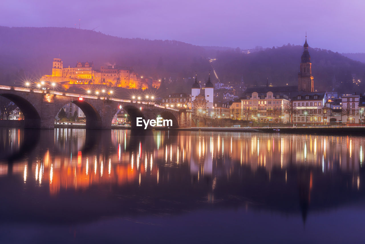 Illuminated buildings by river against sky at night