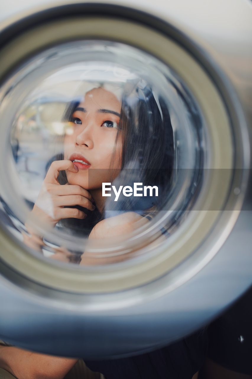 Thoughtful young woman seen through washing machine glass