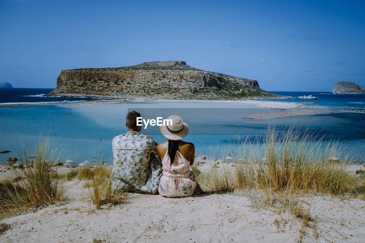 REAR VIEW OF WOMEN AT BEACH AGAINST SKY