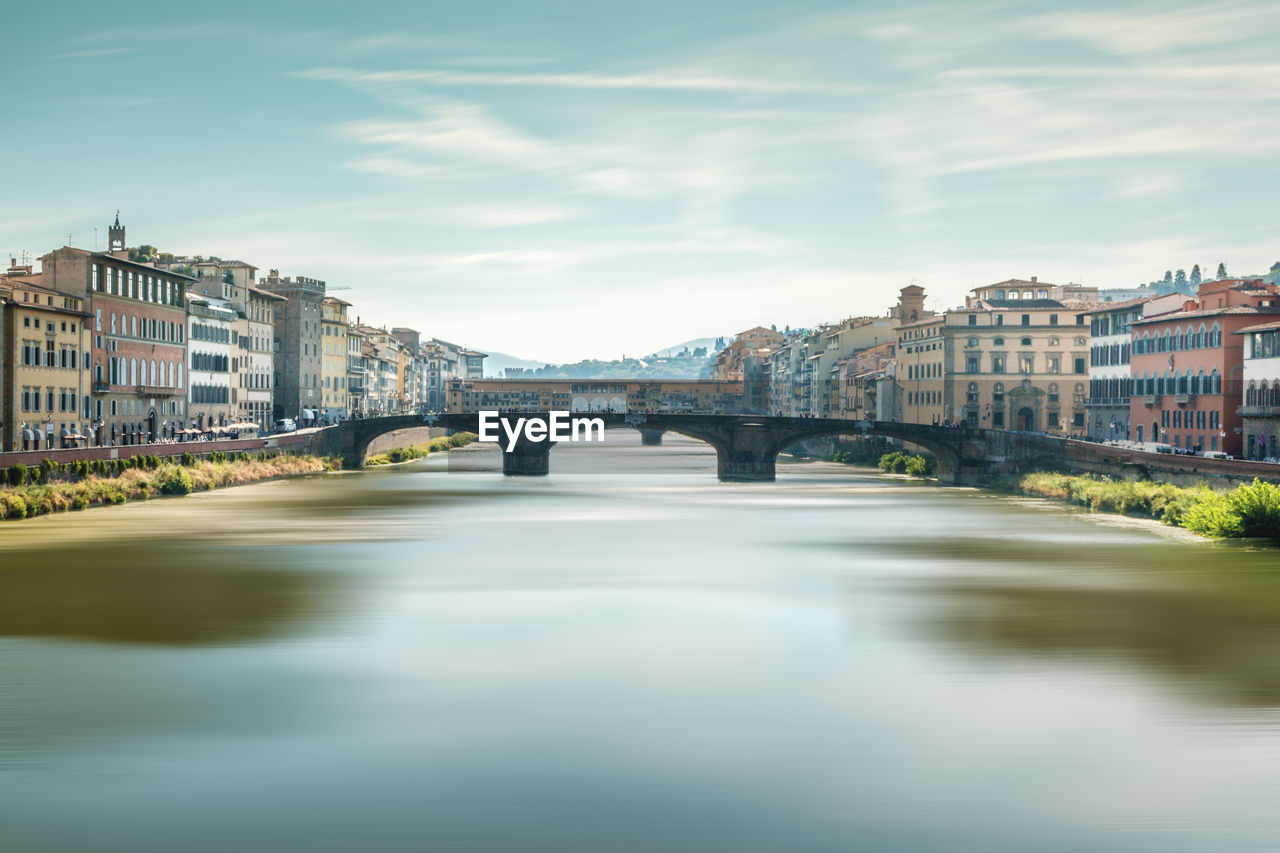 Arch bridge over river amidst buildings in city against sky