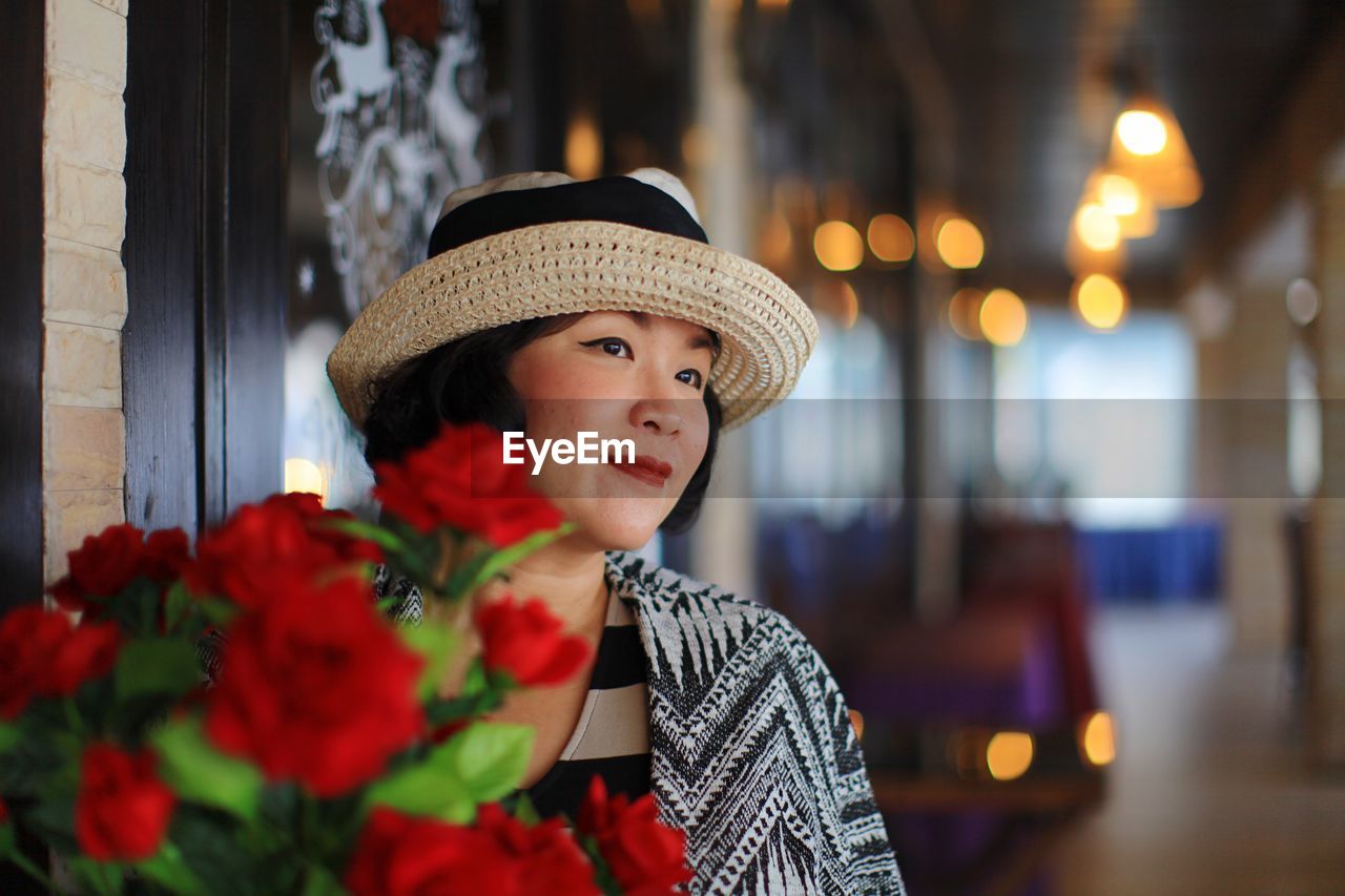 Smiling woman looking away against red flower bouquet