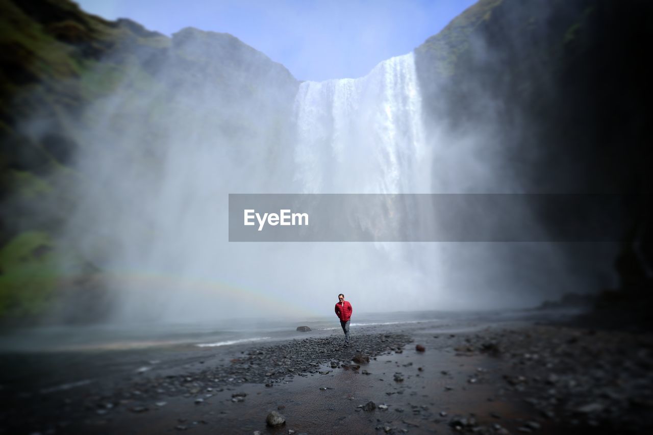 Man walking against waterfall during foggy weather