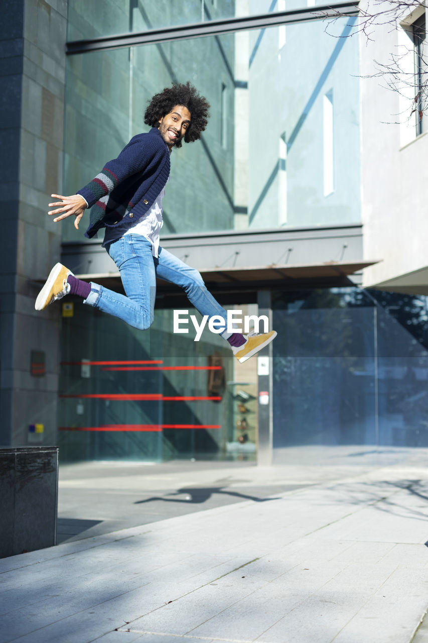 Portrait of man jumping against building in city