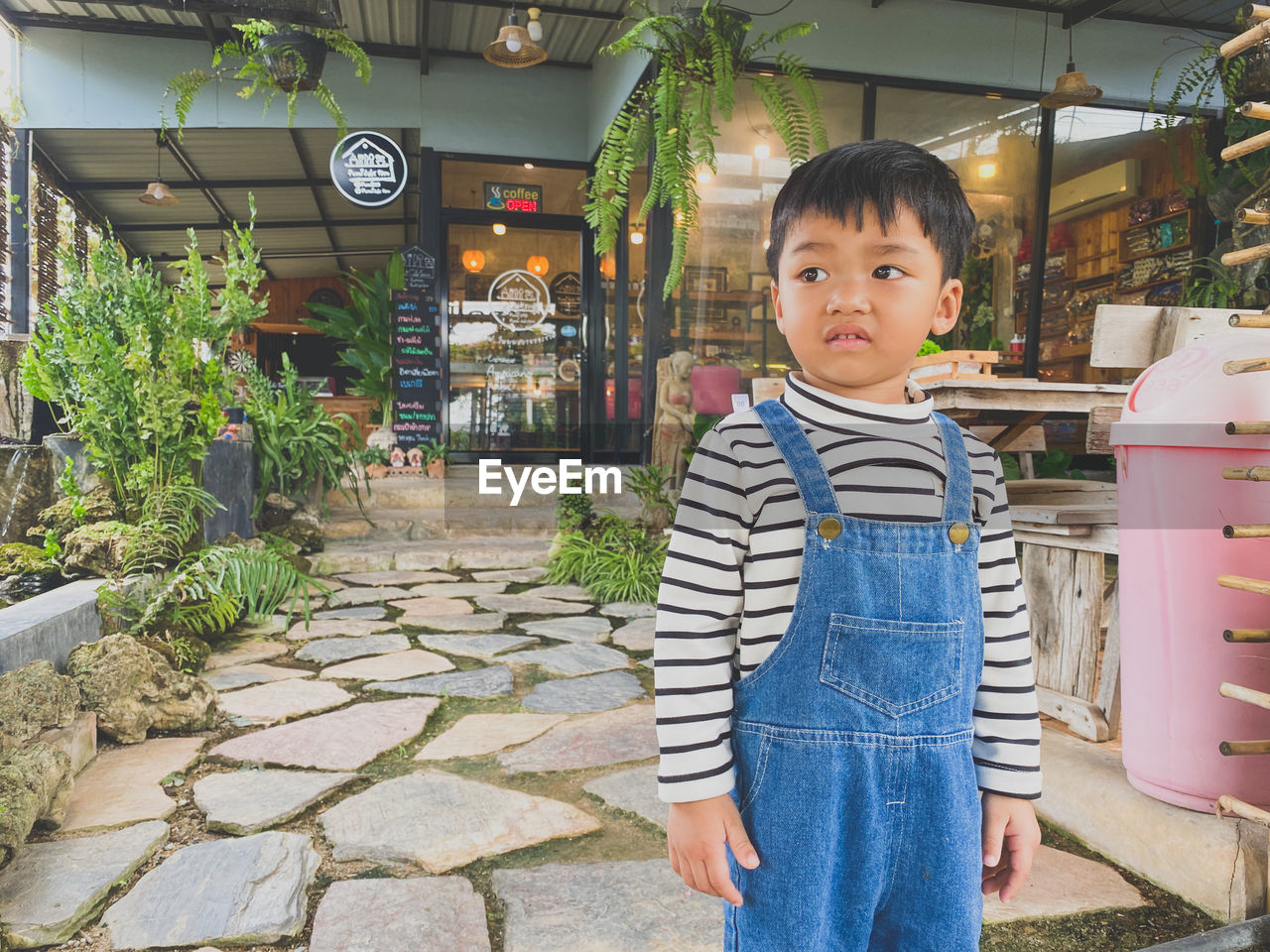 one person, childhood, child, portrait, men, standing, looking at camera, casual clothing, toddler, culture, lifestyles, cute, vacation, innocence, front view, smiling, architecture, outdoors, three quarter length, day, nature, emotion, person, leisure activity, footpath, black hair