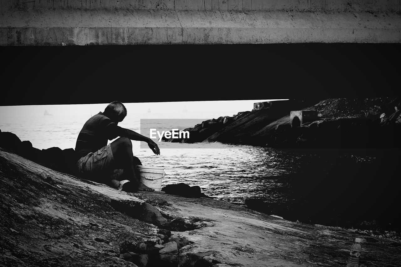 REAR VIEW OF MAN WORKING ON SEA SHORE