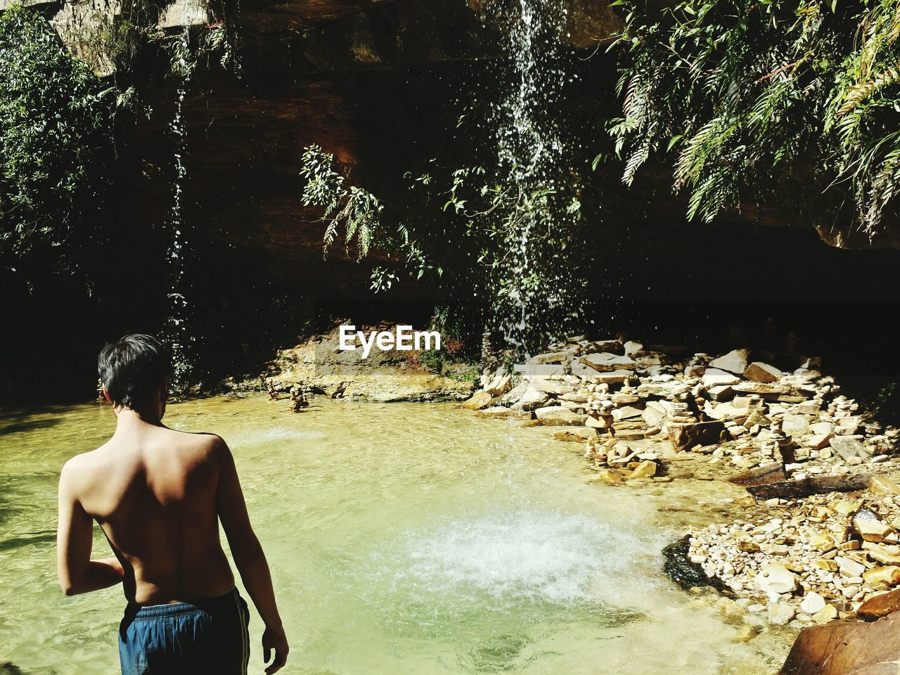 Rear view of shirtless man standing against lake