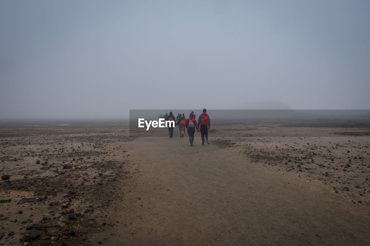 Rear view of people walking on landscape during foggy weather
