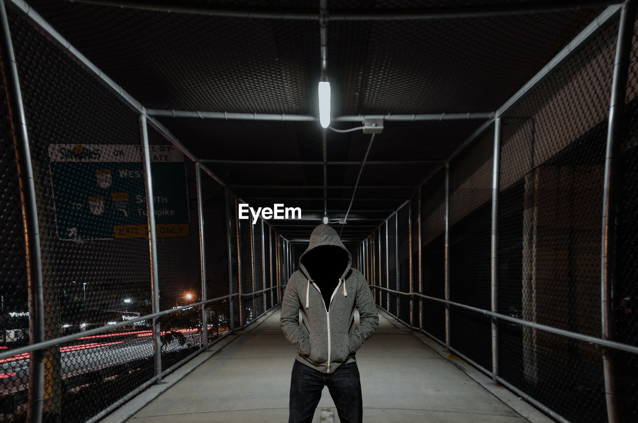 Person wearing hooded shirt standing on footbridge at night