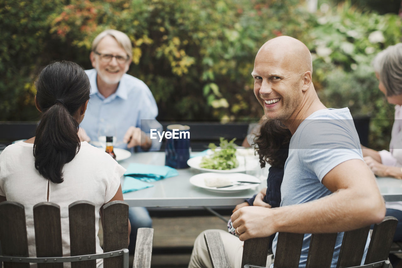 Side view portrait of happy man enjoying meal with family at outdoor table