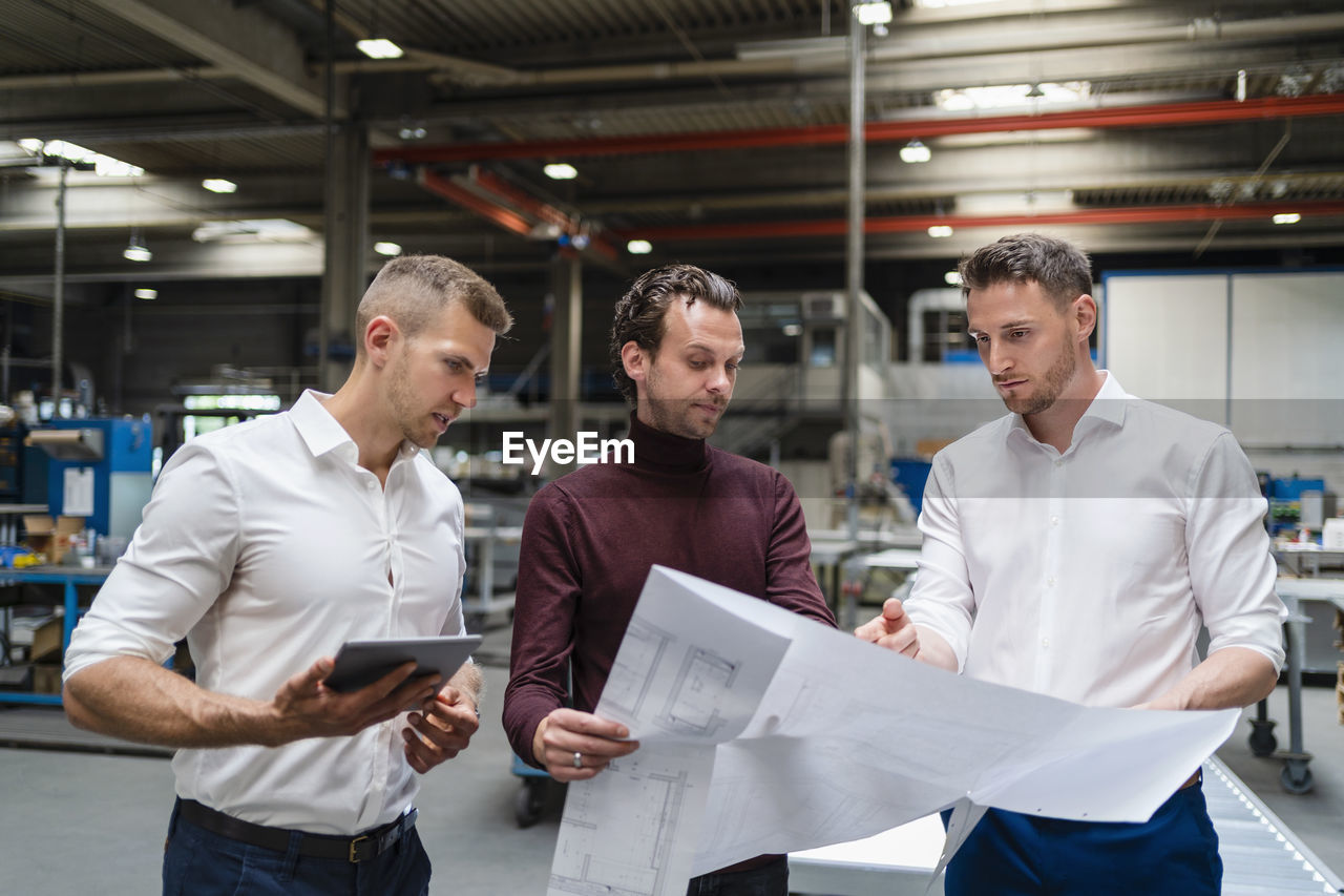 Male professionals discussing over blueprint at factory