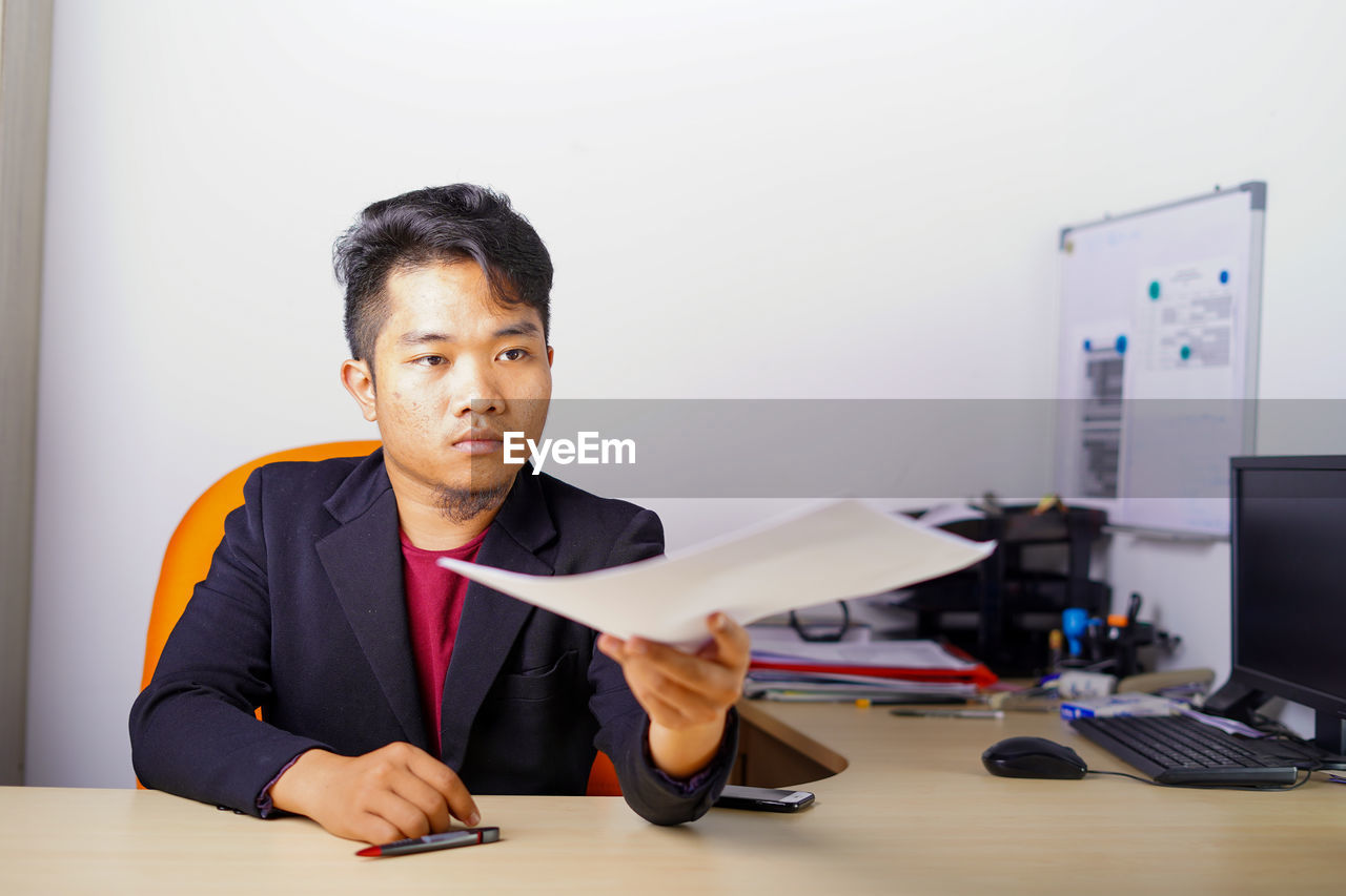 PORTRAIT OF YOUNG MAN WORKING ON TABLE IN OFFICE