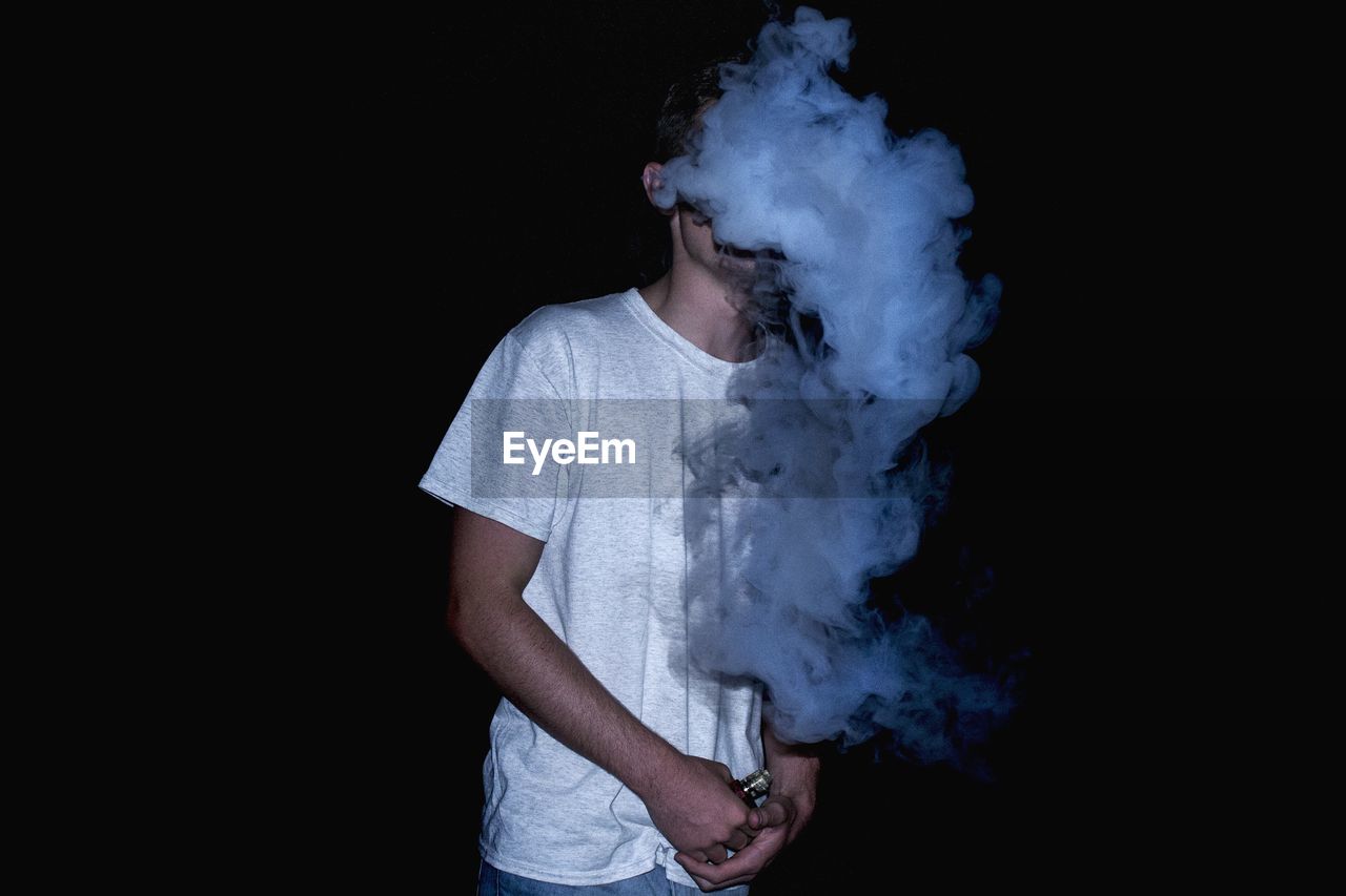 Man emitting smoke while standing against black background