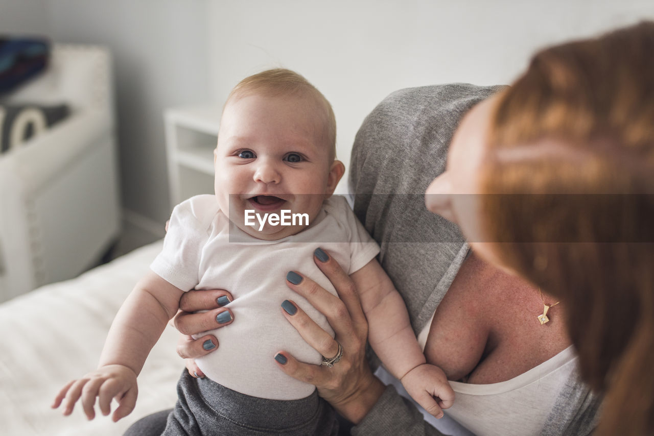 High angle view of mother holding cute son while sitting on bed at home