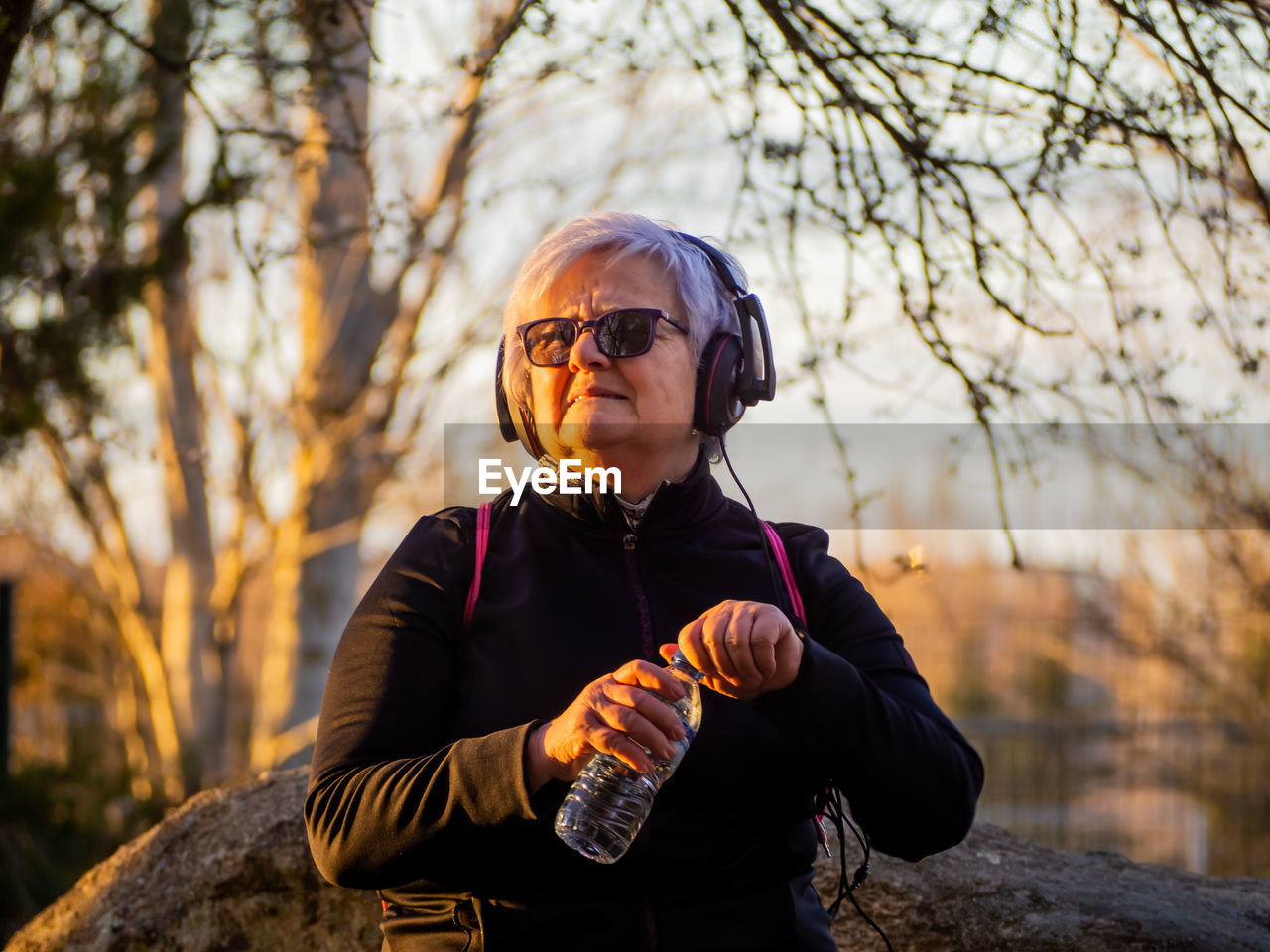 Senior woman listening music in park during sunset