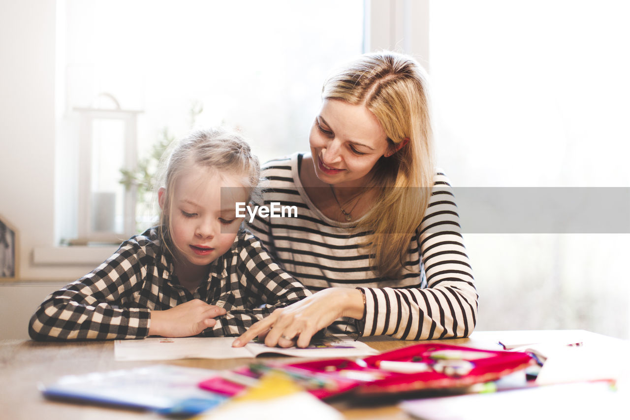 Girl studying while sitting with mother at home