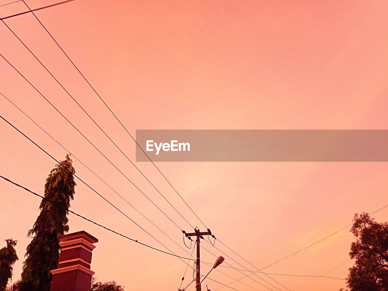 LOW ANGLE VIEW OF SILHOUETTE ELECTRICITY PYLON AGAINST ORANGE SKY