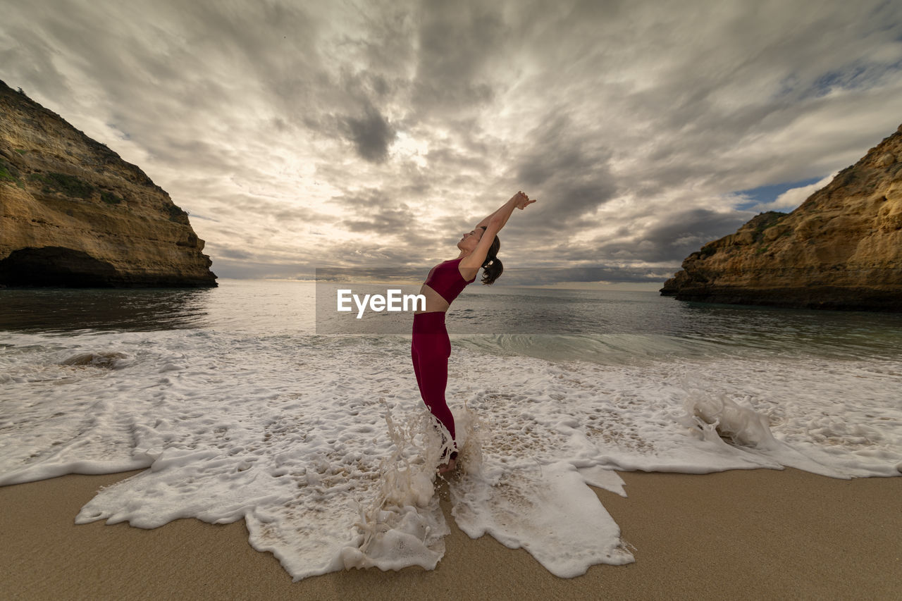 Yoga girl doing a backbend by the sea with a dramatic sky.