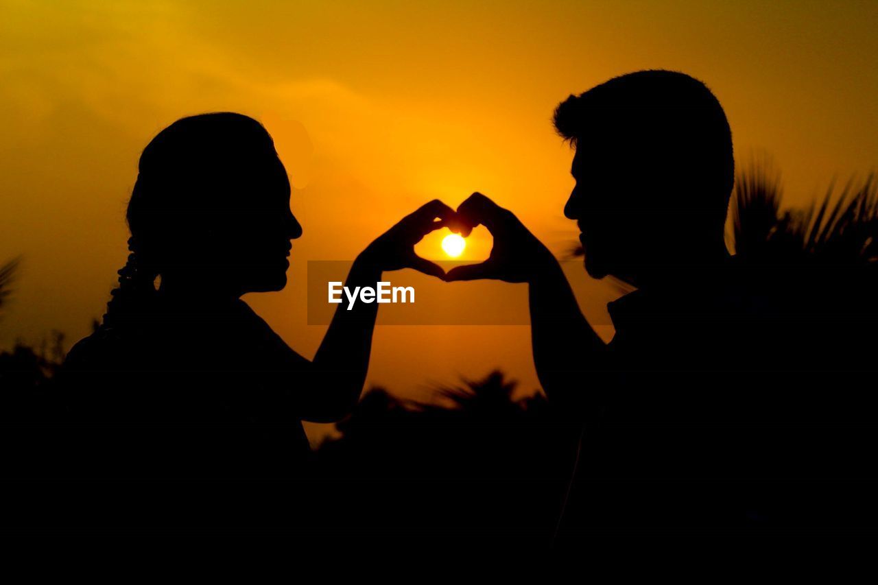 Silhouette couple making heart shape against orange sky