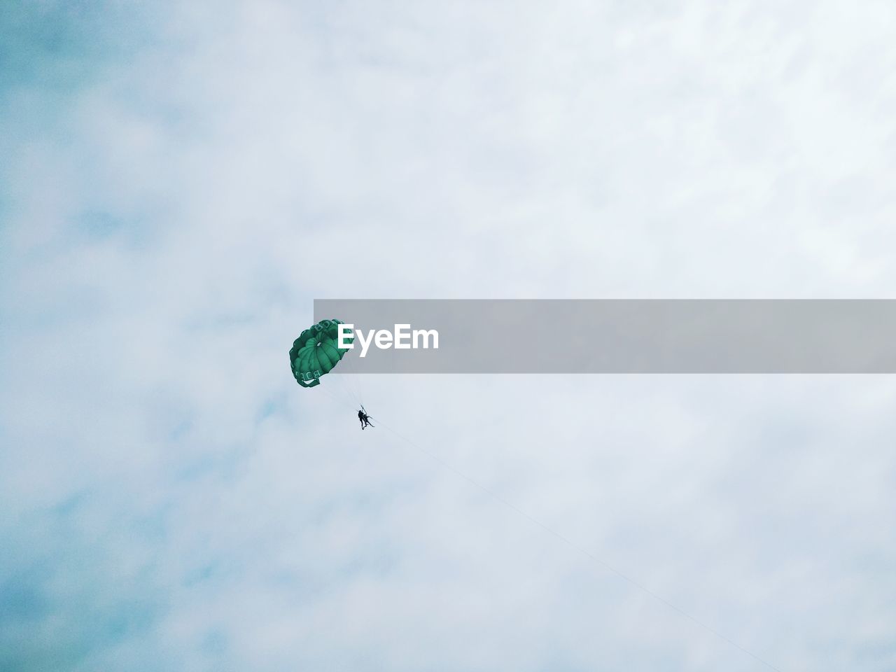 Low angle view of people paragliding against sky