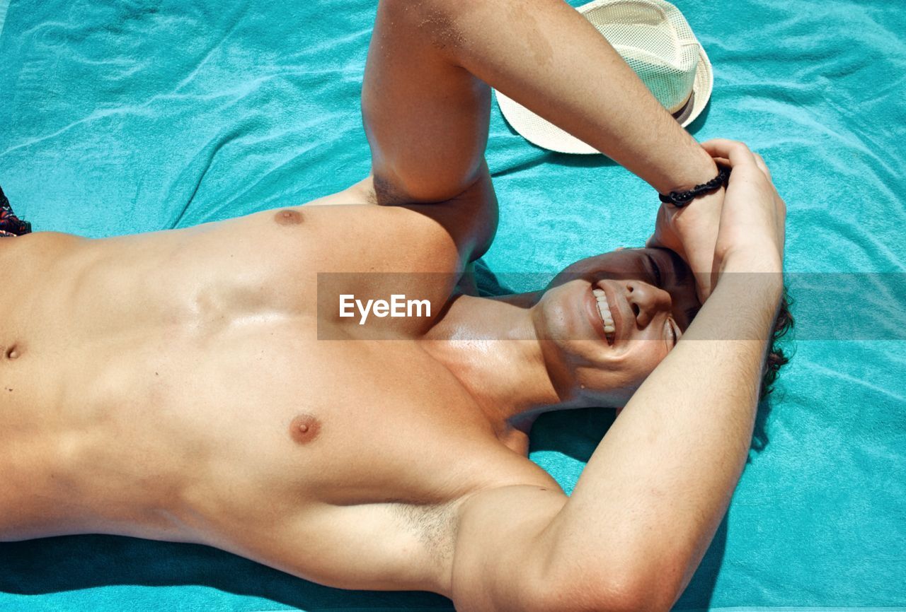 Portrait of shirtless man relaxing at beach in sunny day