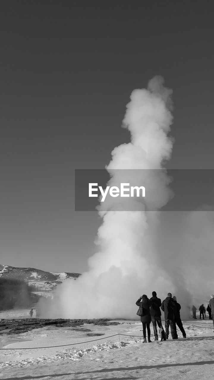 People standing by geyser against sky