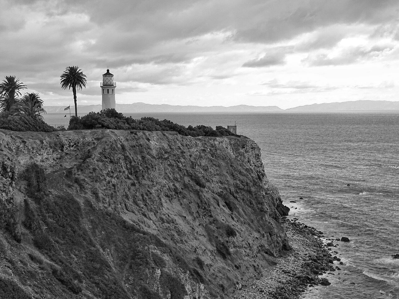 Point vicente lighthouse on cliff by sea against cloudy sky