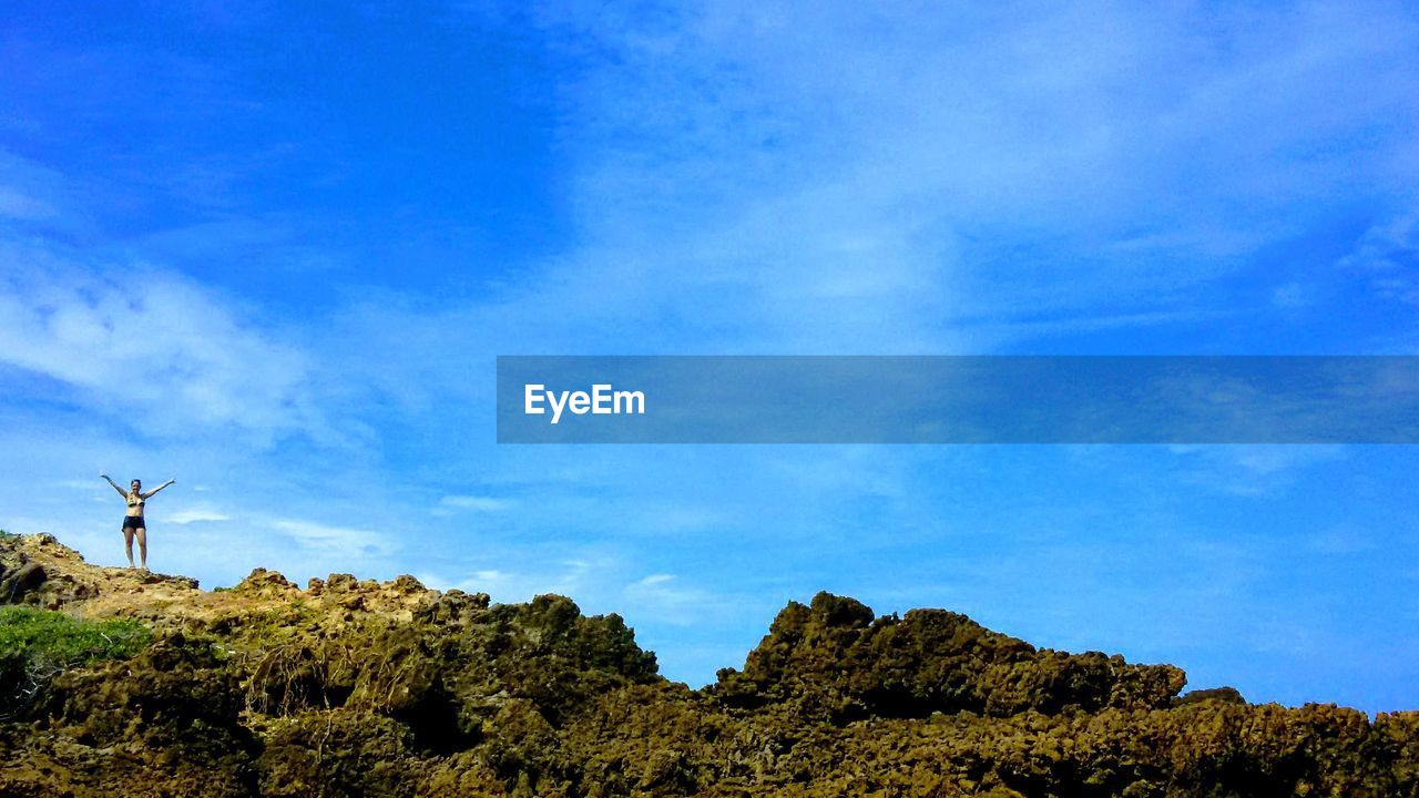 Woman on rocky mountain against blue sky