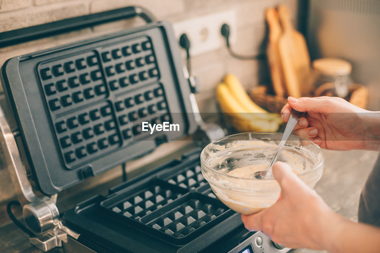 Cropped hands of woman with waffle batter in kitchen