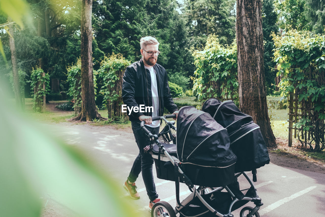 Full length of man pushing baby carriage on footpath