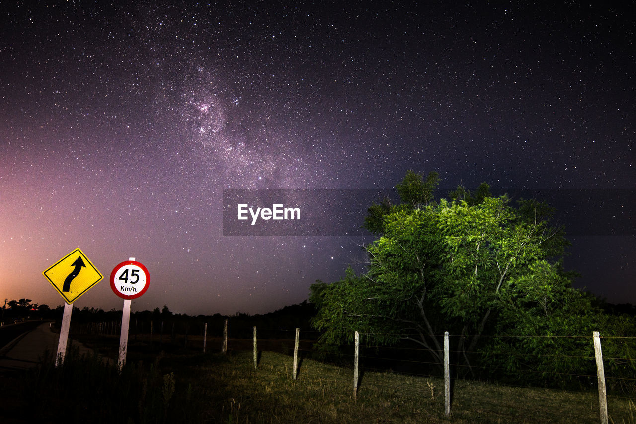 Road sign on field against star field at night