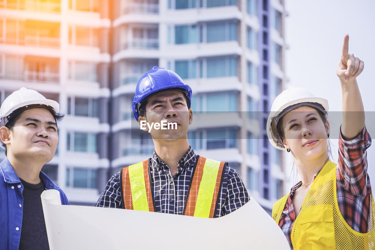 Three engineers discussing over blueprint while standing outdoors