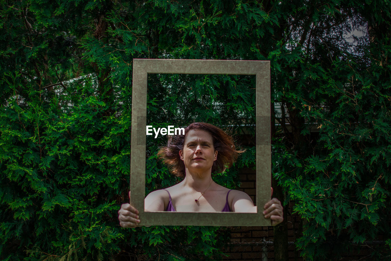 Digital composite of woman holding frame against trees