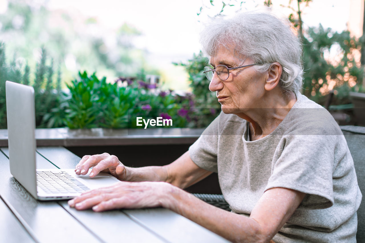 Old woman using laptop on terrace