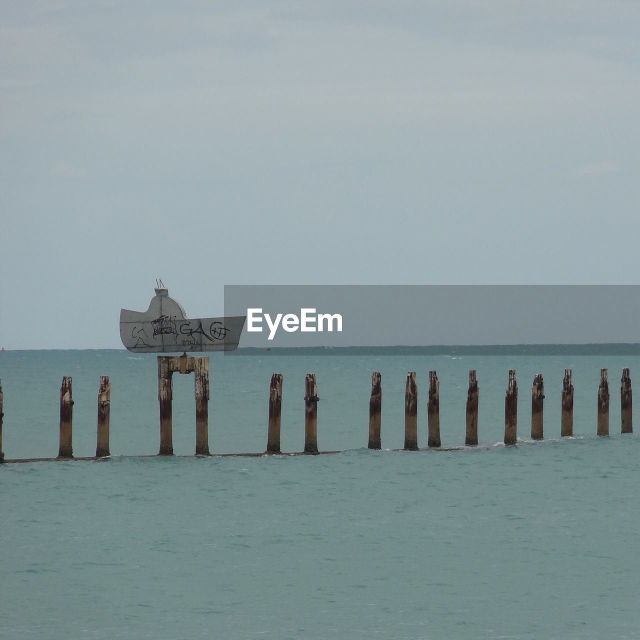 Wooden posts amidst sea against sky