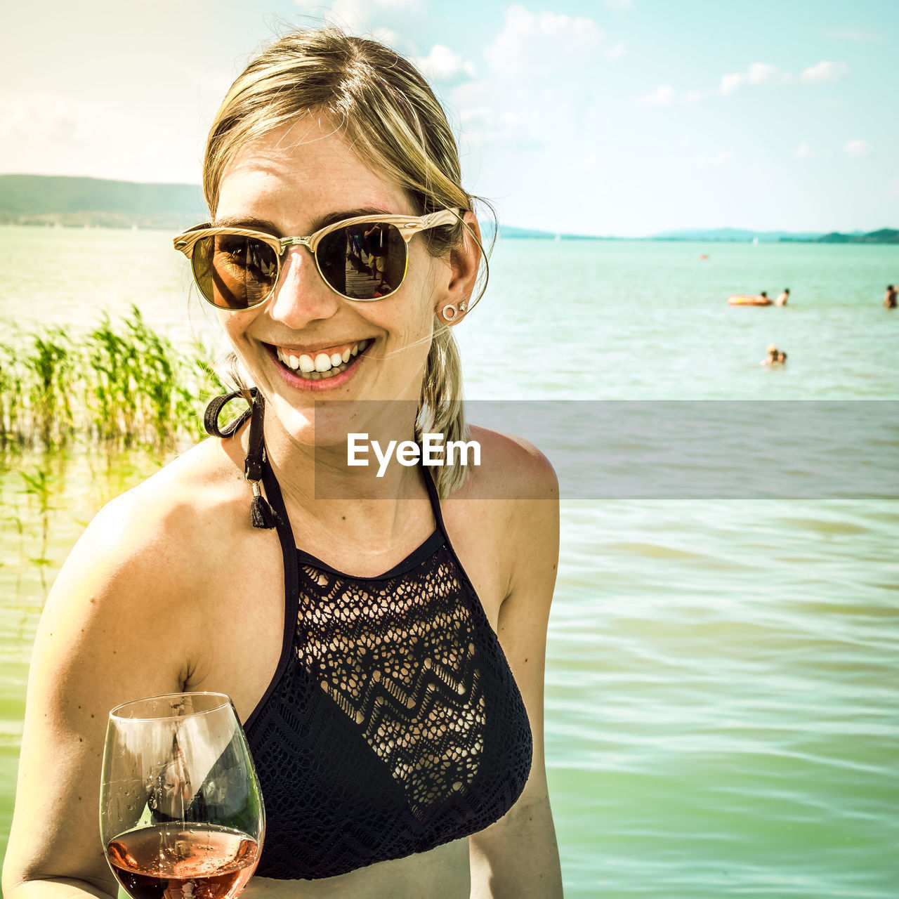 Portrait of smiling young woman wearing sunglasses against lake