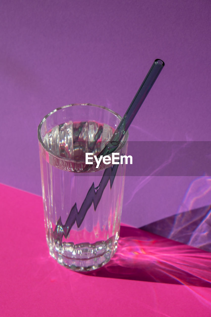 Reusable glass straws in glass with water on purple violet background eco-friendly drinking straw