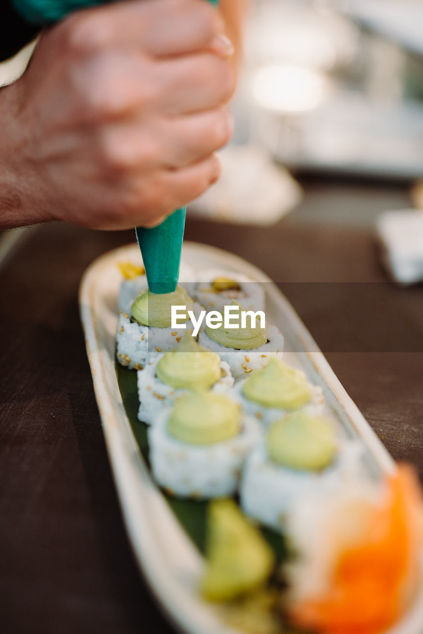 Vertical view of the hands of unknown chief decorating tasty rolls with japanese wasabi sauce