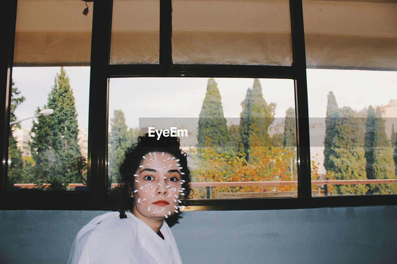 PORTRAIT OF YOUNG WOMAN LOOKING AT WINDOW