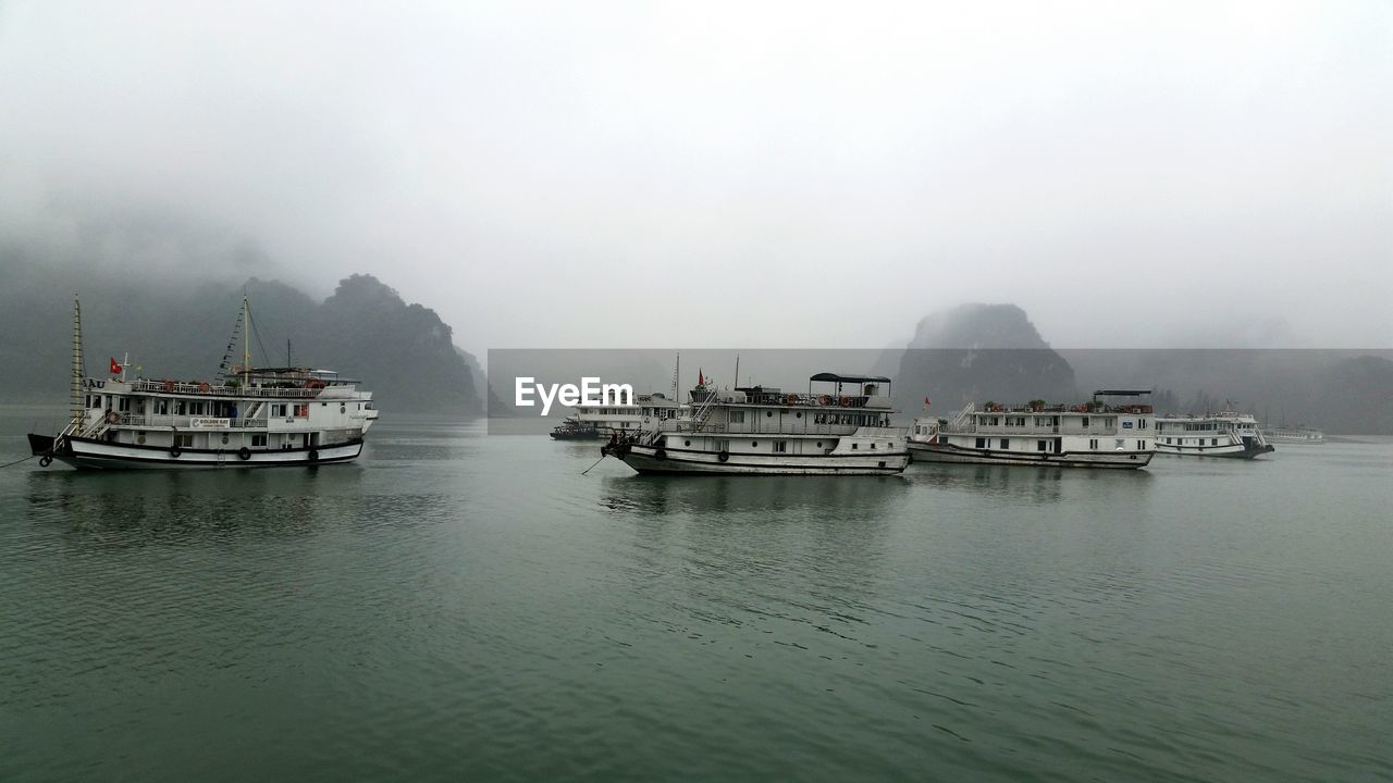 Boats moving on sea against sky during foggy weather
