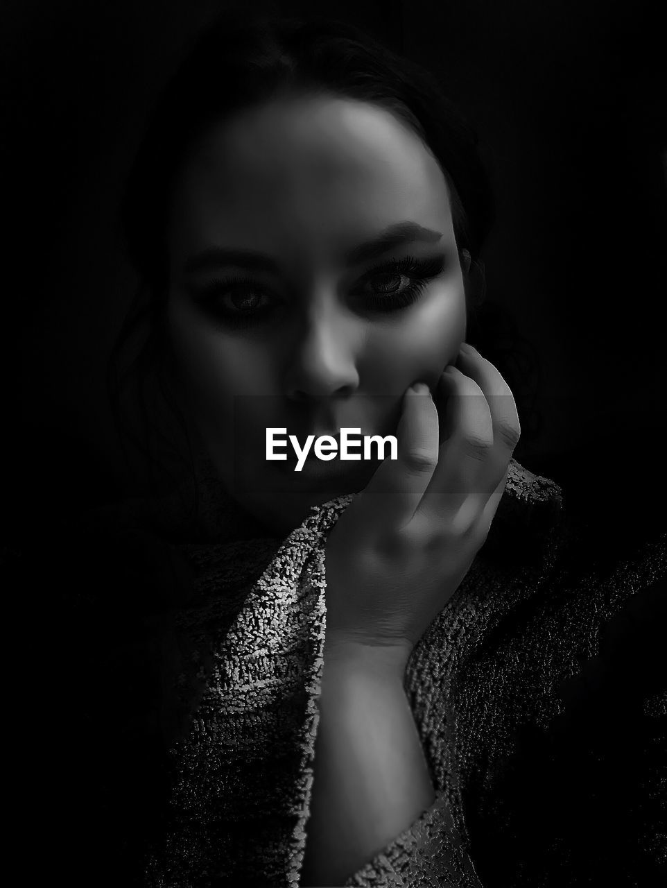 Close-up portrait of young woman with hand on chin against black background