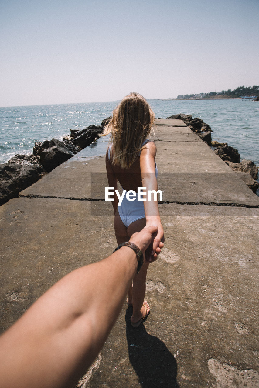 Cropped image of man holding woman hand at beach during sunny day