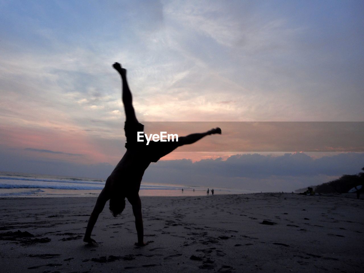 SILHOUETTE WOMAN WITH ARMS RAISED ON BEACH AGAINST SKY
