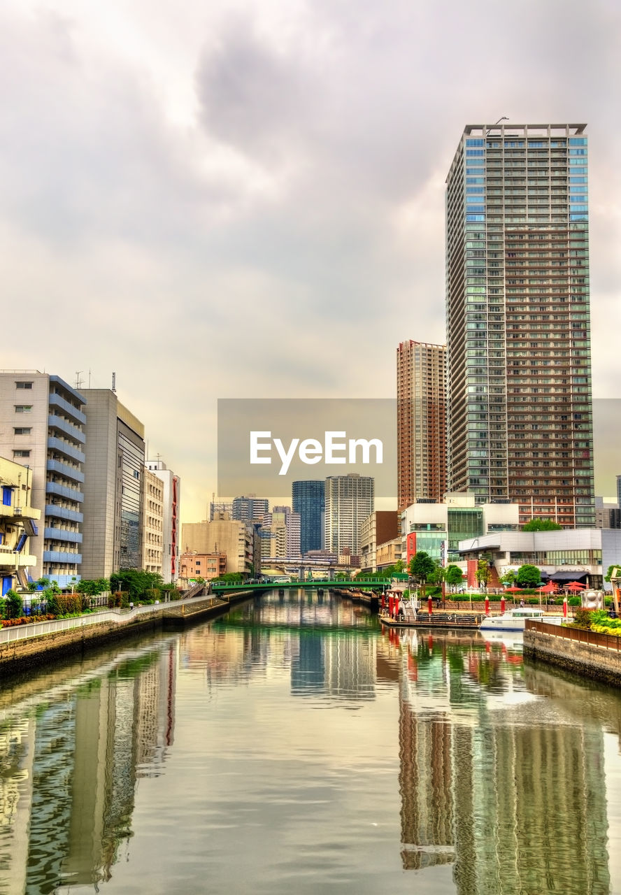 MODERN BUILDINGS BY RIVER AGAINST SKY