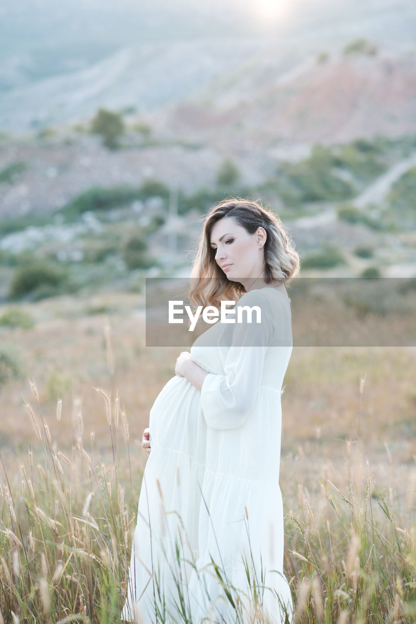 Pregnant woman holding belly standing on field