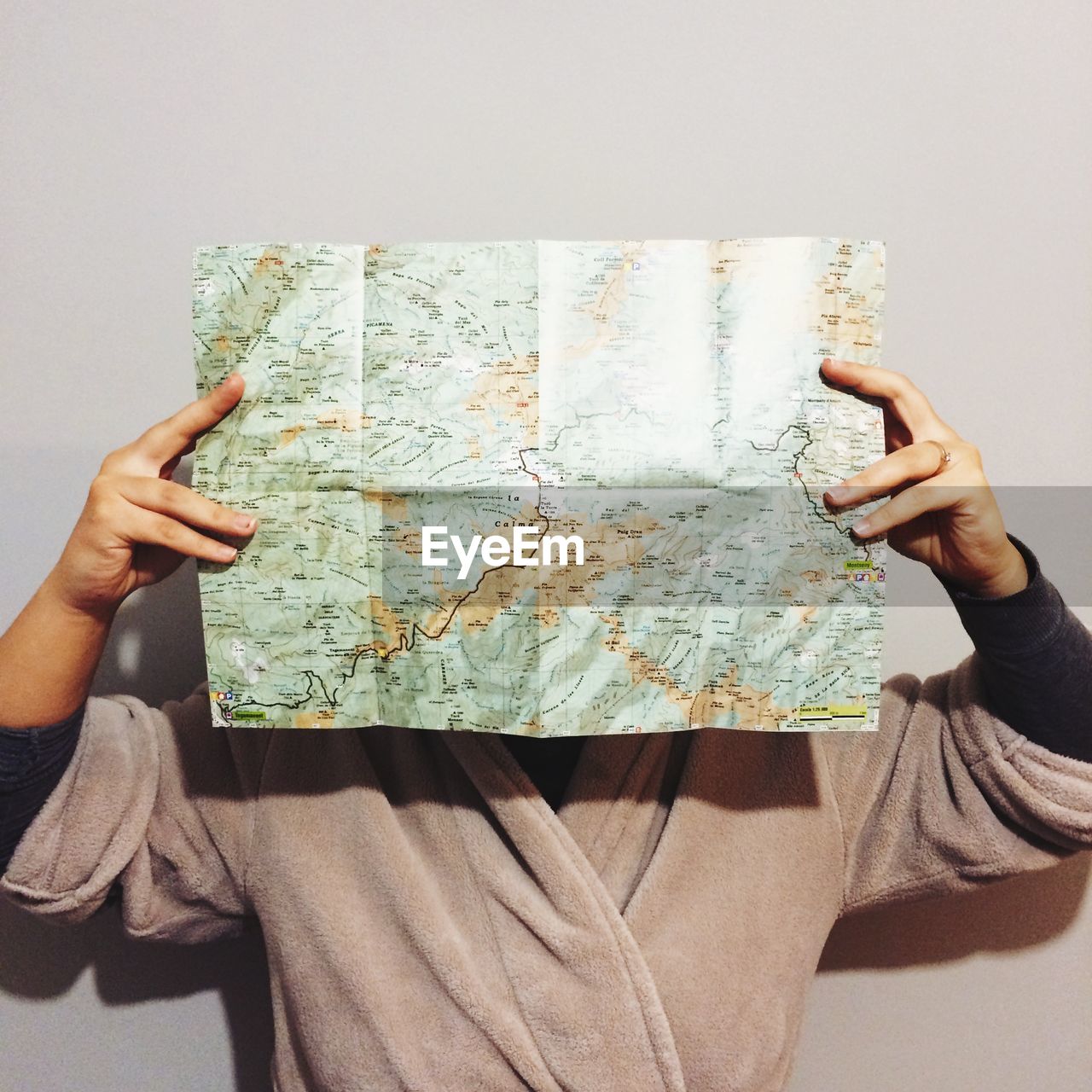 Woman holding map in front of face against wall