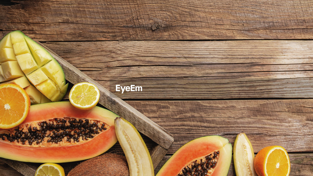 Fresh tropical fruits in a wooden delivery box on a wooden background. papaya, orange, banana