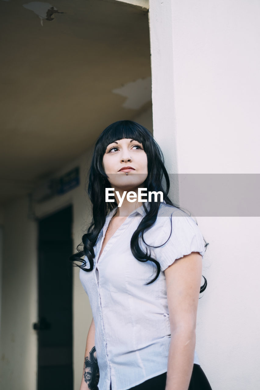 Woman looking away while standing against wall