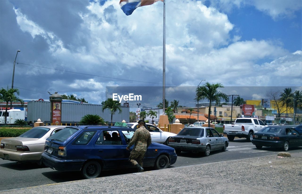 Rear view of man by car on street against cloudy sky